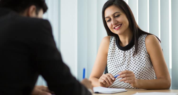 homem de costas assinando papel e mulher sentada à frente sorrindo