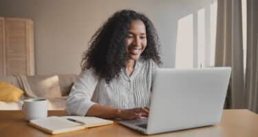 Imagem de uma mulher sorrindo e mexendo no computador para simbolizar como liderar uma equipe