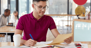 Imagem de um homem de óculos com uma caneta e um papel nas mãos para simbolizar diferença entre estágio e jovem aprendiz