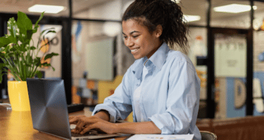 Imagem de uma mulher sorrindo e mexendo no computador para simbolizar recolocação no mercado de trabalho