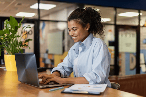 Imagem de uma mulher sorrindo e mexendo no computador para simbolizar recolocação no mercado de trabalho