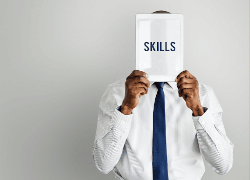Imagem de um homem de terno com uma pape no rosto escrito "skills" para simbolizar o que são Hard skills e soft skills
