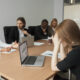Imagem de vários colaboradores em uma mesa de reunião conversando e uma mulher com a cabeça baixa para simbolizar a fofoca no trabalho